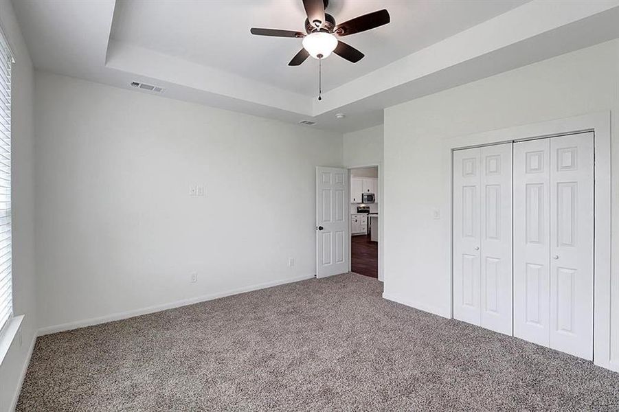 Unfurnished bedroom featuring carpet floors, a raised ceiling, and ceiling fan