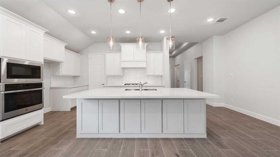 Kitchen with stainless steel appliances, hanging light fixtures, a kitchen island with sink, and light wood-type flooring