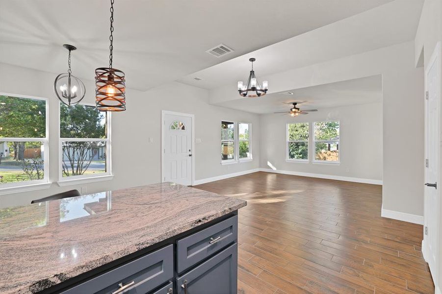 Kitchen with light stone counters, dark wood-type flooring, ceiling fan with notable chandelier, and pendant lighting