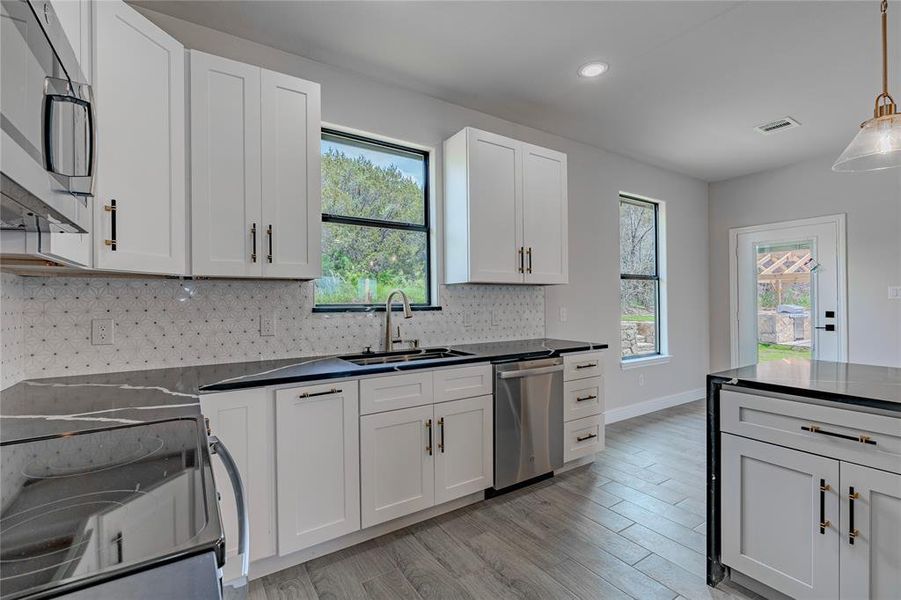 Kitchen with stainless steel appliances, light wood-type flooring, pendant lighting, backsplash, and sink