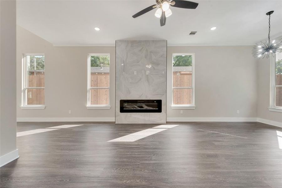 Unfurnished living room featuring dark wood-type flooring, ceiling fan with notable chandelier, and a fireplace