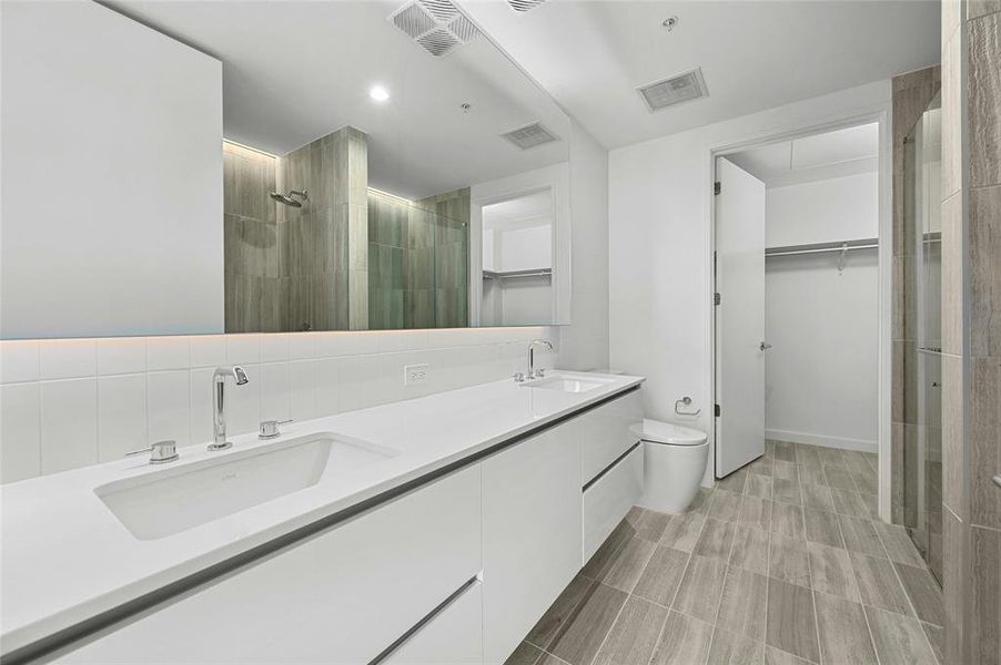 The primary bathroom showcases a dual vanity with sleek white cabinets, providing ample storage & a modern aesthetic plus a large horizontal mirror, enhancing the spacious feel and functionality of the area. *Linden Residence No. 2105 Shown Here