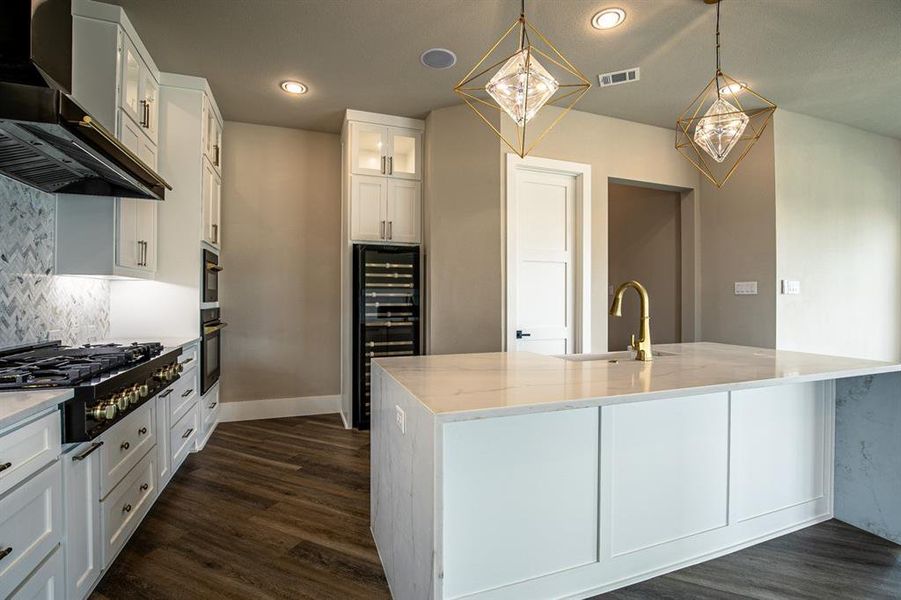 Kitchen featuring white cabinets, backsplash, wall chimney exhaust hood and large island