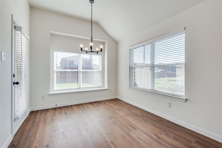 Unfurnished dining area featuring hardwood / wood-style flooring, a healthy amount of sunlight, an inviting chandelier, and vaulted ceiling