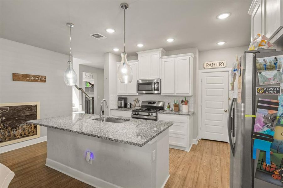 Kitchen with decorative light fixtures, white cabinets, sink, light hardwood / wood-style floors, and appliances with stainless steel finishes