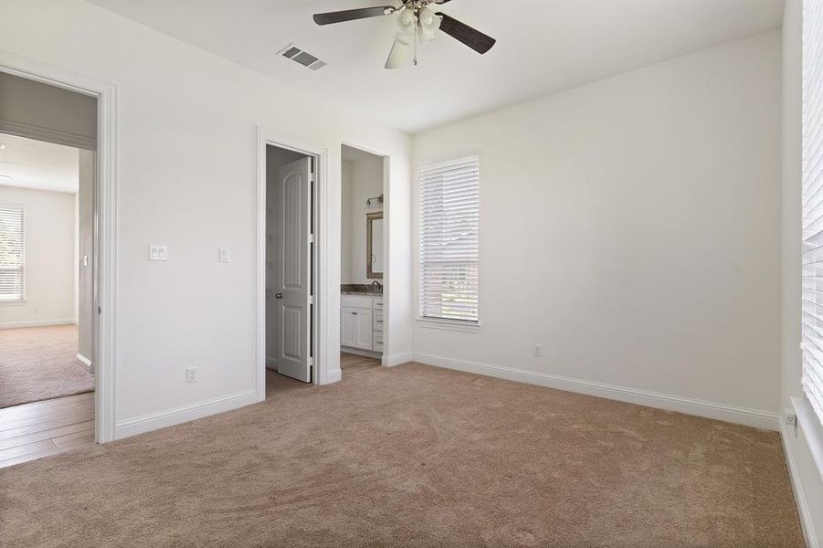 Unfurnished bedroom featuring multiple windows, ceiling fan, connected bathroom, and light colored carpet