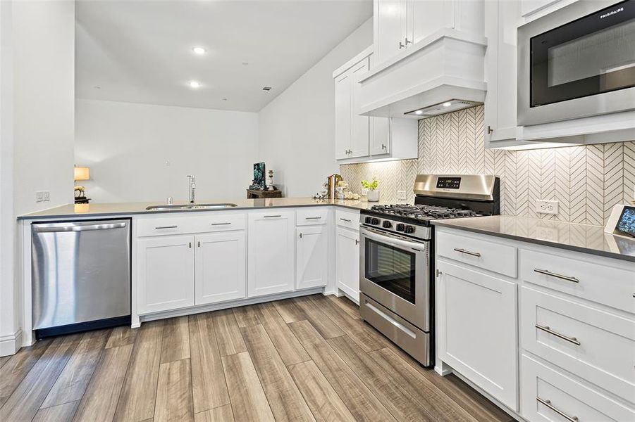 Kitchen with light hardwood / wood-style flooring, premium range hood, sink, appliances with stainless steel finishes, and white cabinets