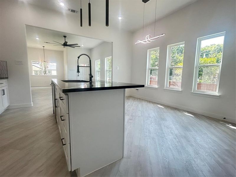 Kitchen with white cabinetry, light hardwood / wood-style flooring, ceiling fan with notable chandelier, and a kitchen island with sink