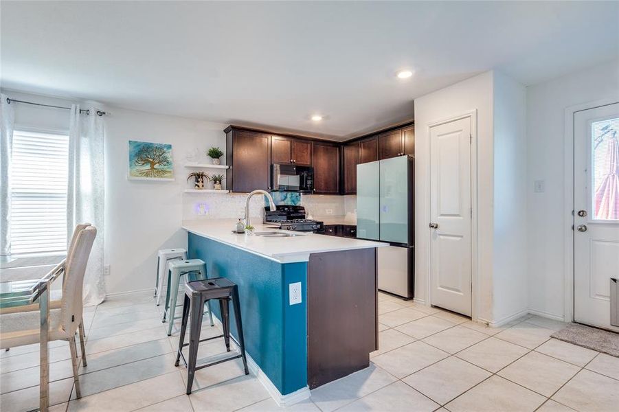 Kitchen featuring dark brown cabinets, a breakfast bar, kitchen peninsula, black appliances, and tasteful backsplash