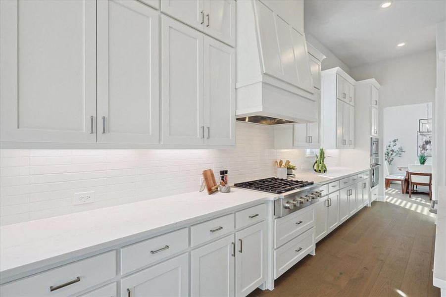 Kitchen featuring premium range hood, backsplash, dark wood-type flooring, white cabinetry, and stainless steel gas stovetop