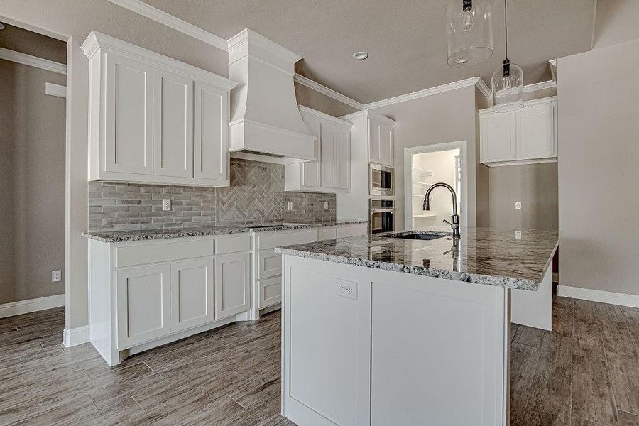 Kitchen featuring appliances with stainless steel finishes, a center island with sink, sink, backsplash, and custom exhaust hood