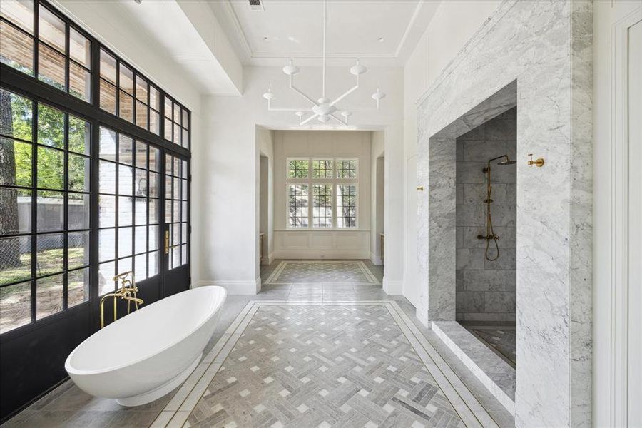 The primary bathroom exudes opulence. It features a beautiful porcelain soaking tub, elegant marble flooring, a chic chandelier, and spacious marble shower.