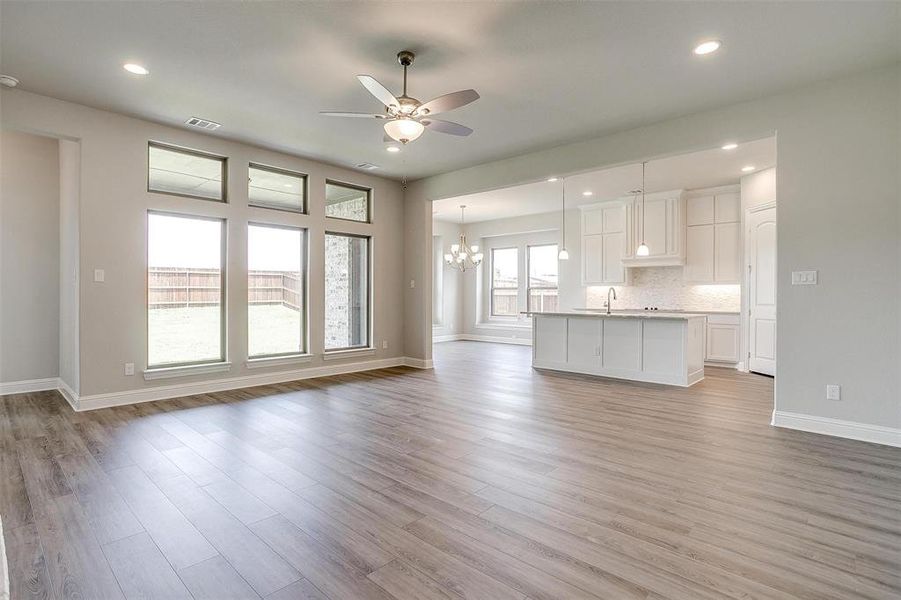 Unfurnished living room with sink, ceiling fan with notable chandelier, and light hardwood / wood-style floors