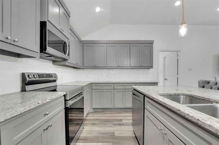 Kitchen featuring light hardwood / wood-style floors, decorative light fixtures, appliances with stainless steel finishes, and gray cabinets