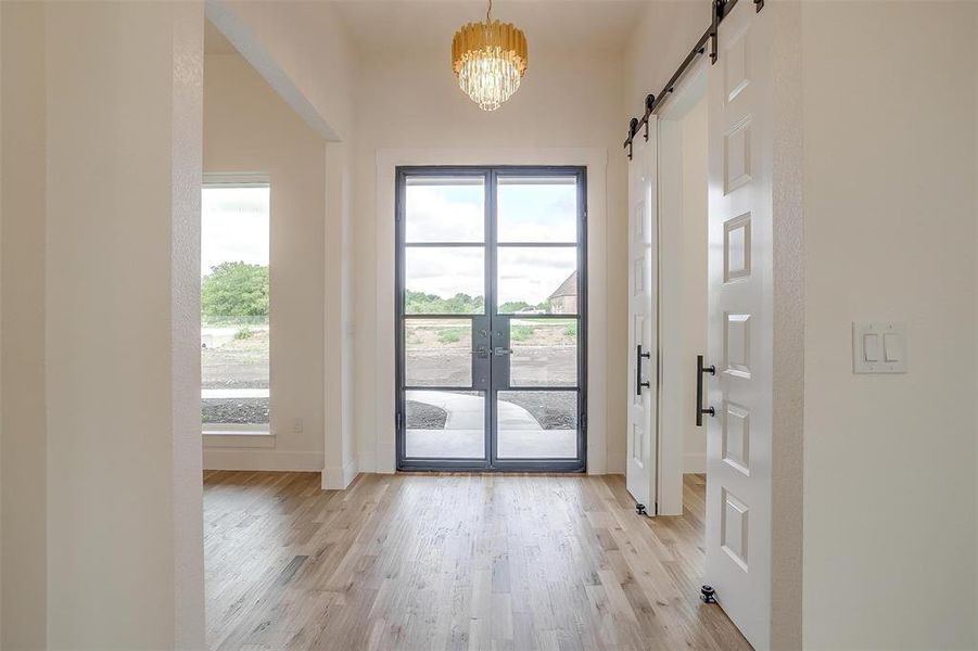 Doorway with a chandelier, light hardwood / wood-style flooring, a barn door, and french doors