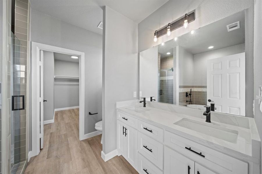 Bathroom featuring hardwood / wood-style flooring, double sink vanity, toilet, and an enclosed shower