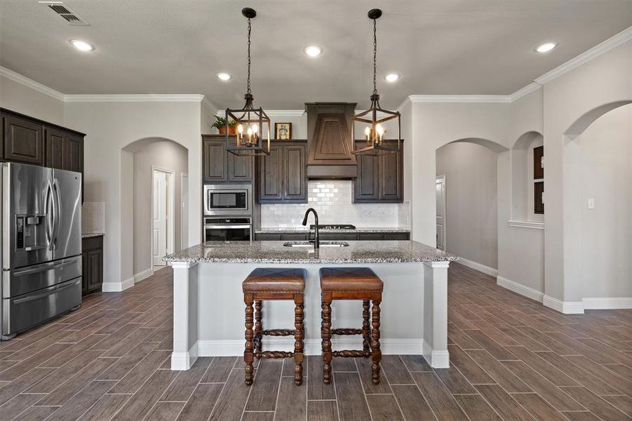 Kitchen with crown molding, decorative light fixtures, backsplash, sink, and appliances with stainless steel finishes