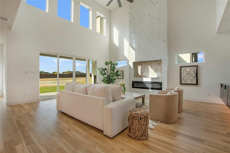 Living room with a large fireplace, light hardwood / wood-style floors, a towering ceiling, and ceiling fan