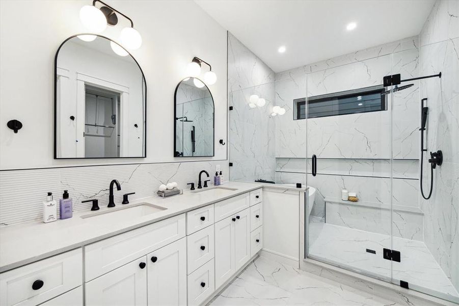 Primary Bath with a 12 x 24 Tile Floor, Shaker Style Cabinetry with Soft Close Drawers and Doors. Slab Quartz Counter, 12 x 24 Textured Tile Backsplash. Dual Rectangle Sinks, Widespread Bathroom Faucets, Framed Mirrors and Dual Two Globe Lights Finished in Black.