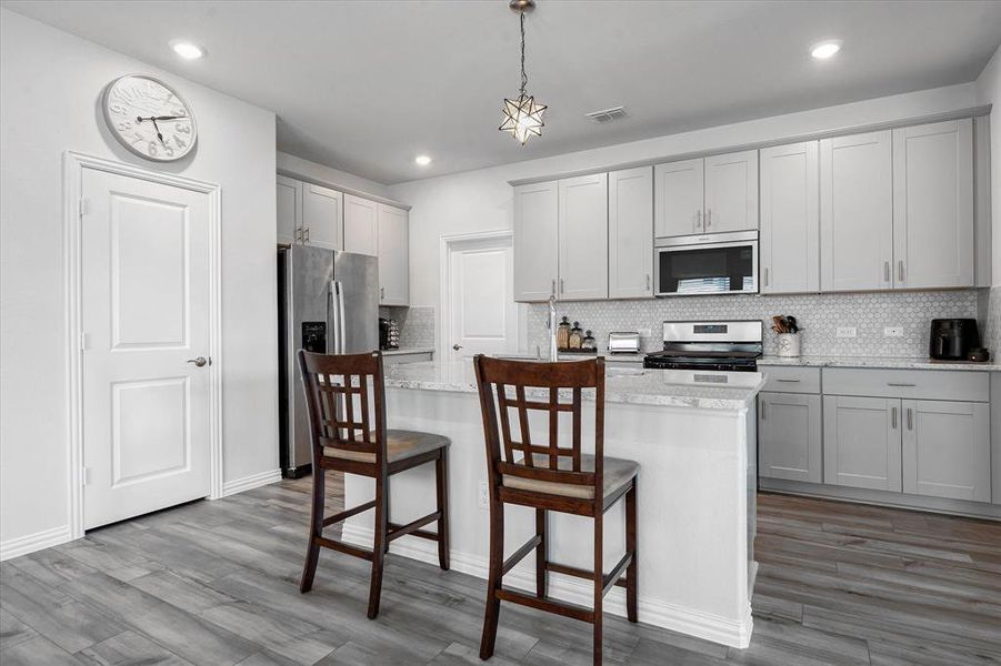 Kitchen with light wood-type flooring, a center island, light stone counters, appliances with stainless steel finishes, and backsplash