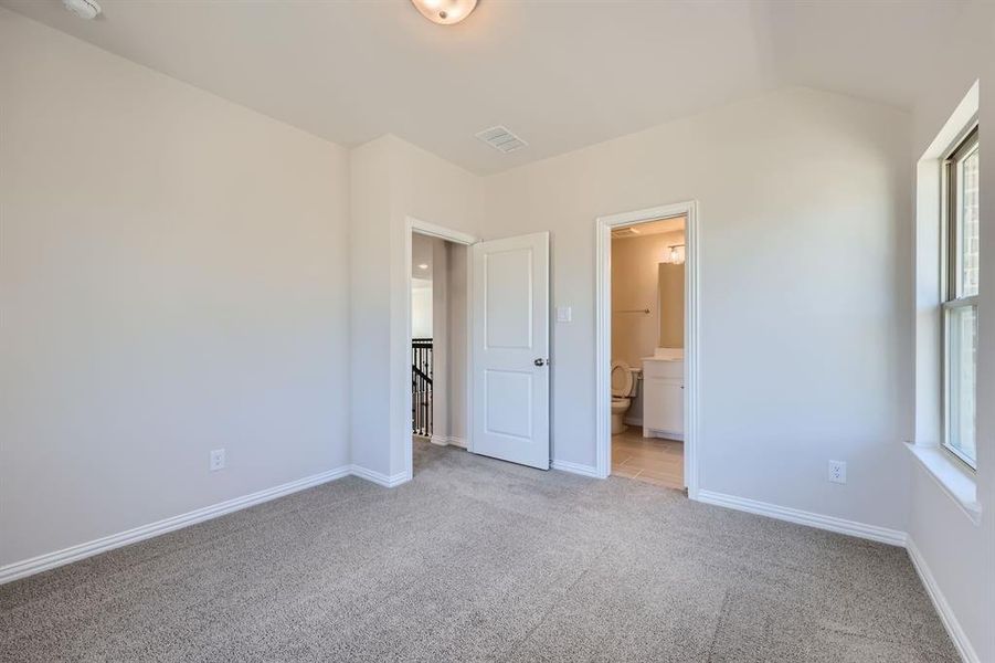 Bedroom with light carpet, multiple windows, connected bathroom, and lofted ceiling