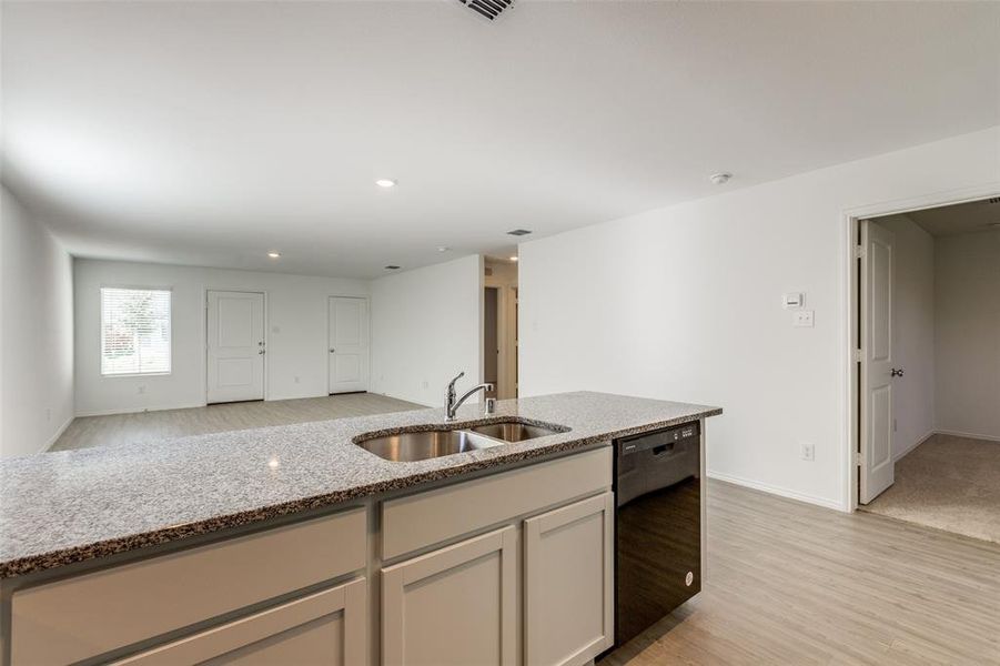 Kitchen with light stone countertops, dishwasher, light hardwood / wood-style flooring, and sink