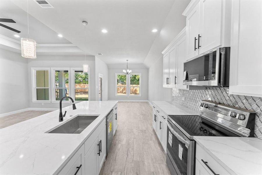 Kitchen with sink, white cabinetry, appliances with stainless steel finishes, decorative light fixtures, and light stone countertops