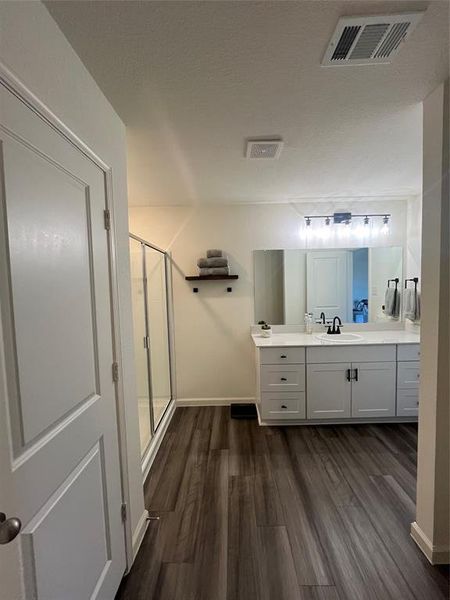 Bathroom featuring vanity, a textured ceiling, walk in shower, and wood-type flooring