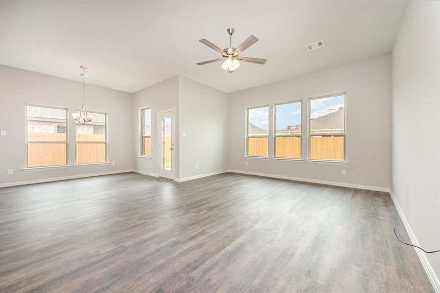 Unfurnished living room with dark hardwood / wood-style floors, ceiling fan with notable chandelier, and a wealth of natural light