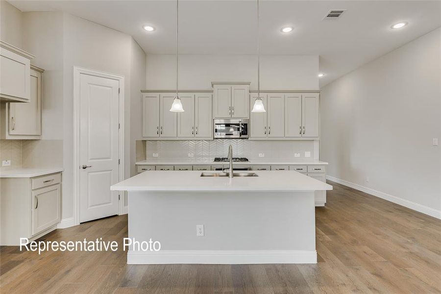 Kitchen featuring decorative light fixtures, light hardwood / wood-style flooring, decorative backsplash, and a center island with sink