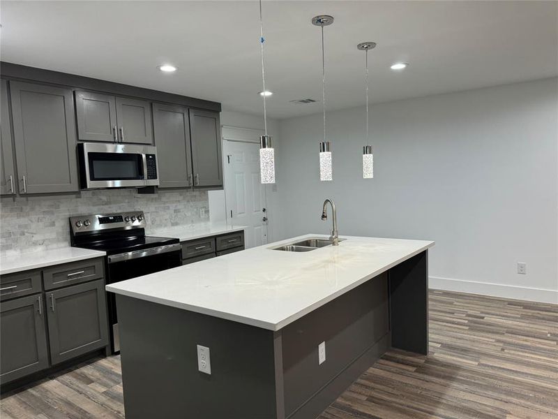 Kitchen with a center island with sink, pendant lighting, appliances with stainless steel finishes, dark wood-type flooring, and sink