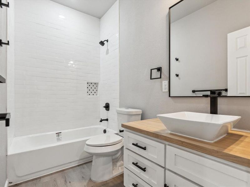 Full bathroom with hardwood / wood-style floors, toilet, tiled shower / bath combo, and vanity