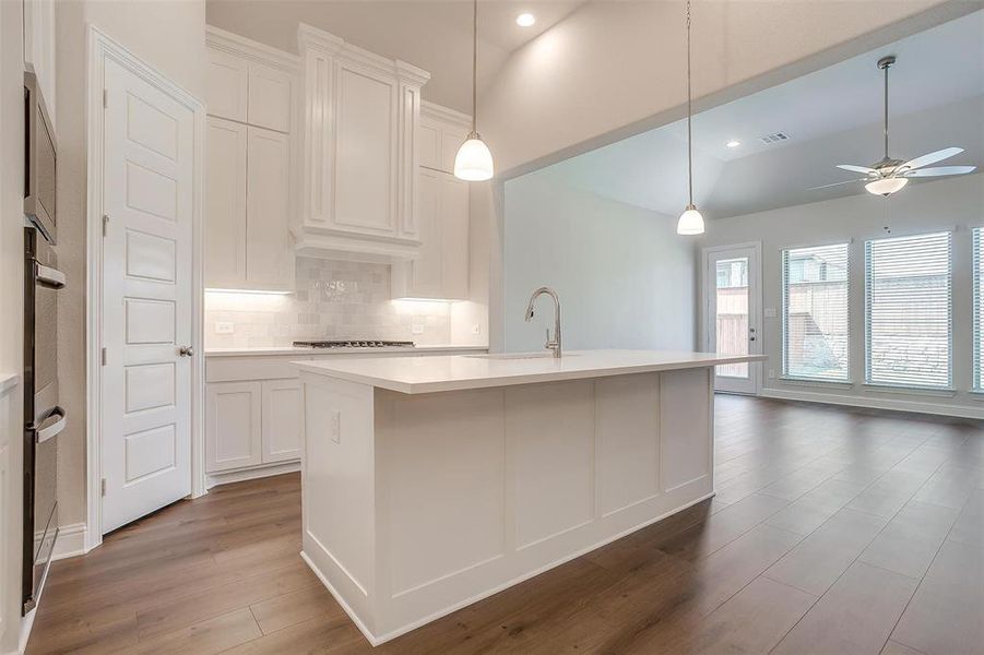 Kitchen with decorative backsplash, an island with sink, ceiling fan, hardwood / wood-style flooring, and hanging light fixtures