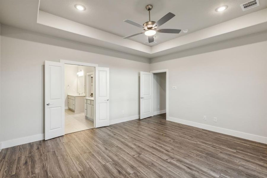 Unfurnished bedroom featuring a raised ceiling, hardwood / wood-style floors, ensuite bathroom, and ceiling fan