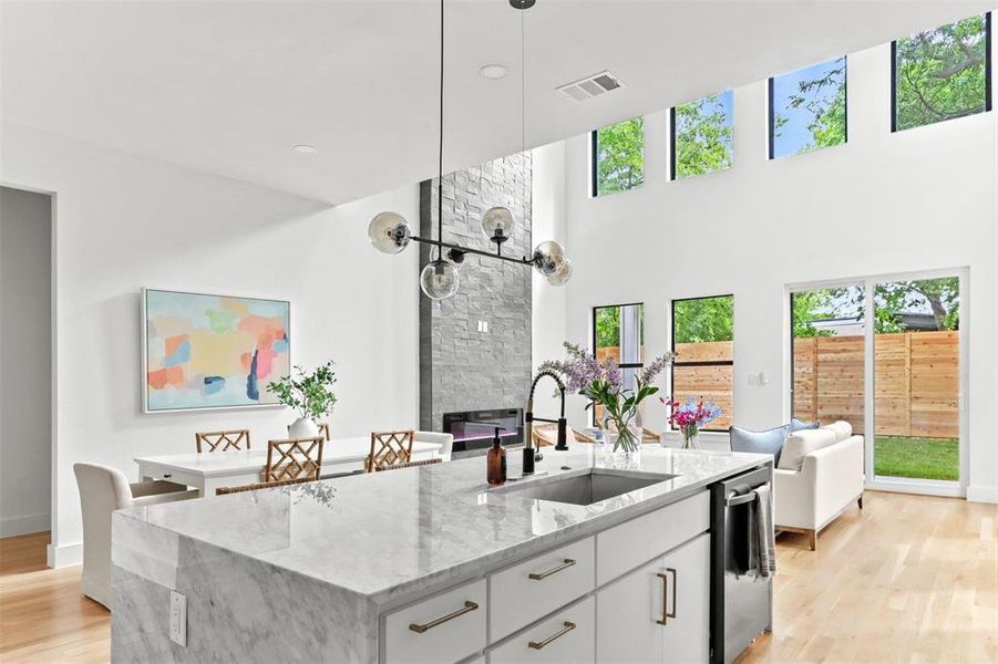 Kitchen featuring light hardwood / wood-style flooring, light stone counters, sink, an island with sink, and a stone fireplace