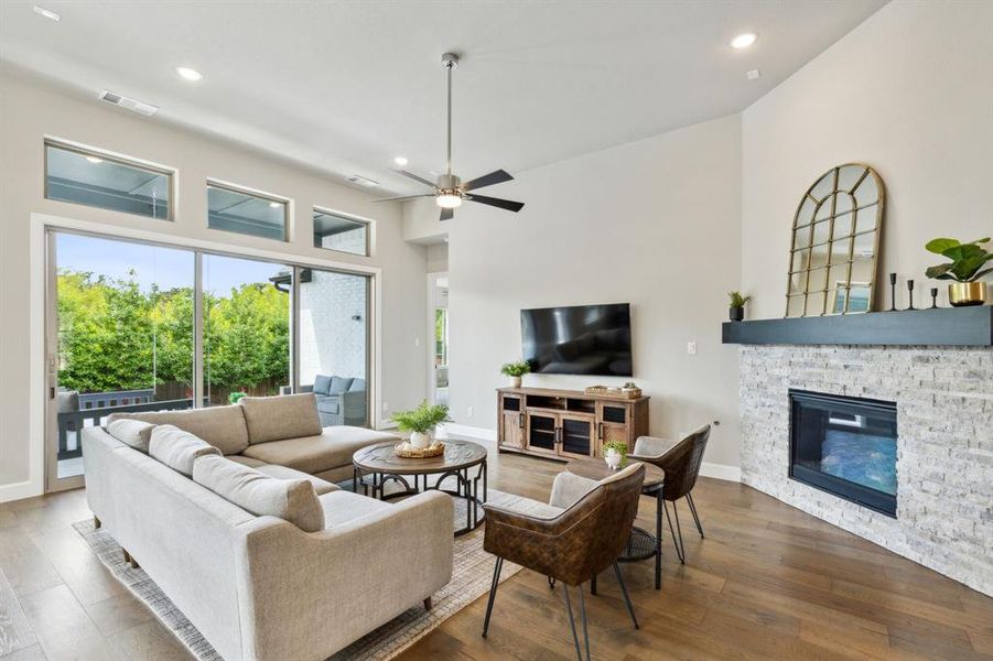 Living room featuring high vaulted ceiling, ceiling fan, a stone fireplace, and wood-type flooring