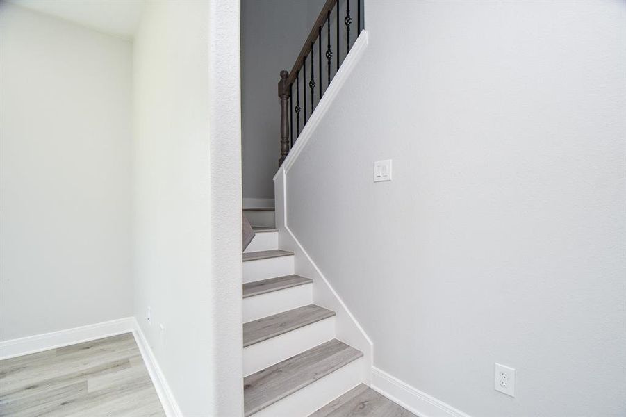 This is a clean, modern staircase with white walls and gray wood-look flooring, featuring a classic black metal baluster railing.