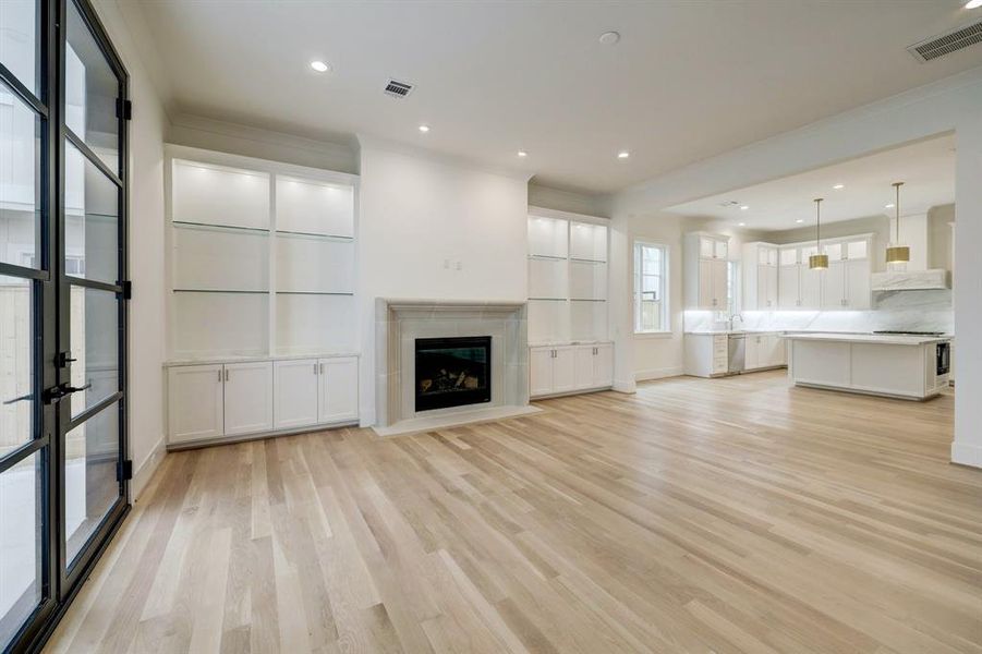 The living area features beautiful custom built-in cabinetry with recessed lighting, glass shelving and a marble countertop that flanks the fireplace with stone surround and gas logs.