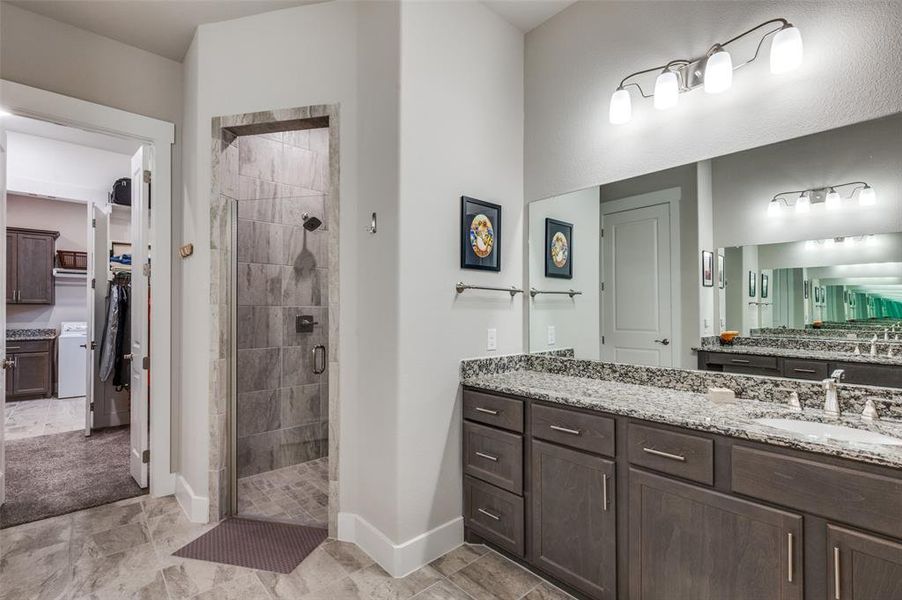 Primary bathroom with dual granite topped vanities, tile shower, tile flooring