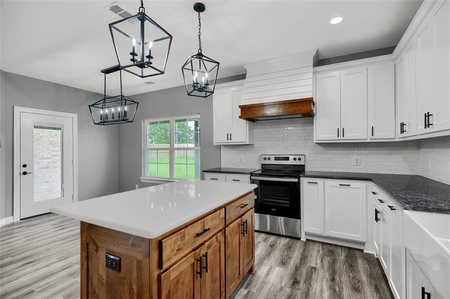 Kitchen with a center island, light hardwood / wood-style floors, stainless steel range with electric cooktop, custom range hood, and decorative light fixtures