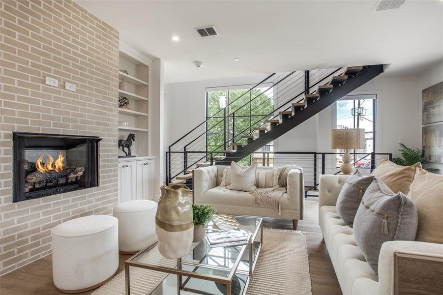 Living room with wood- flooring, built in features, a brick gas fireplace, and a wealth of natural light