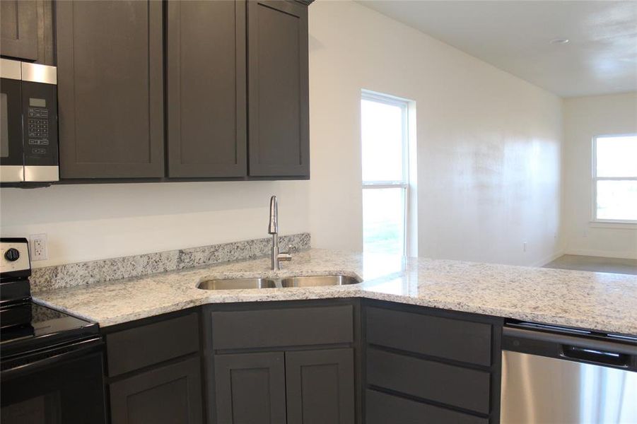 Kitchen with light stone counters, sink, stainless steel appliances, and plenty of natural light