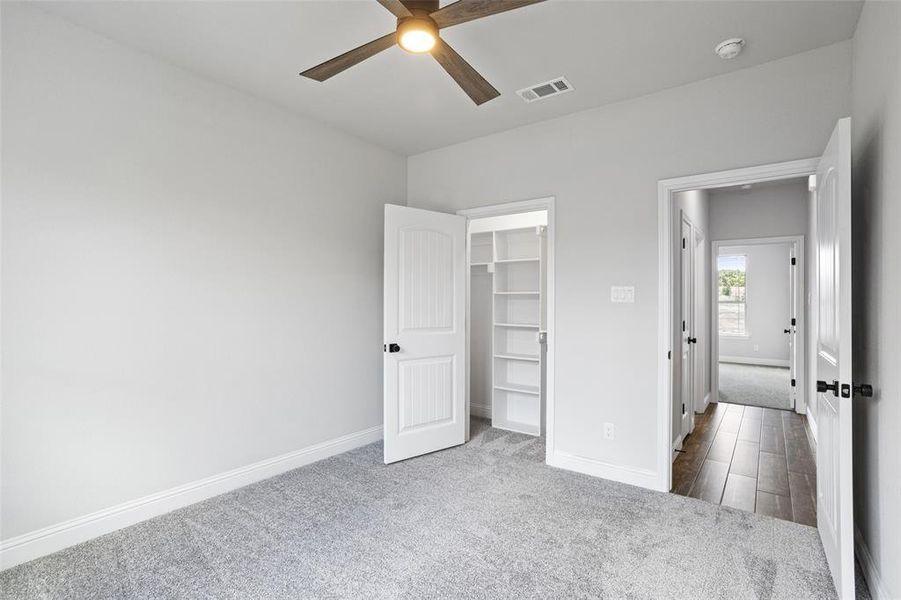 Unfurnished bedroom with a walk in closet, ceiling fan, carpet flooring, and a closet