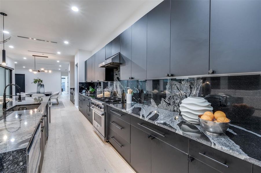 Kitchen with tasteful backsplash, sink, light wood-type flooring, hanging light fixtures, and high end range