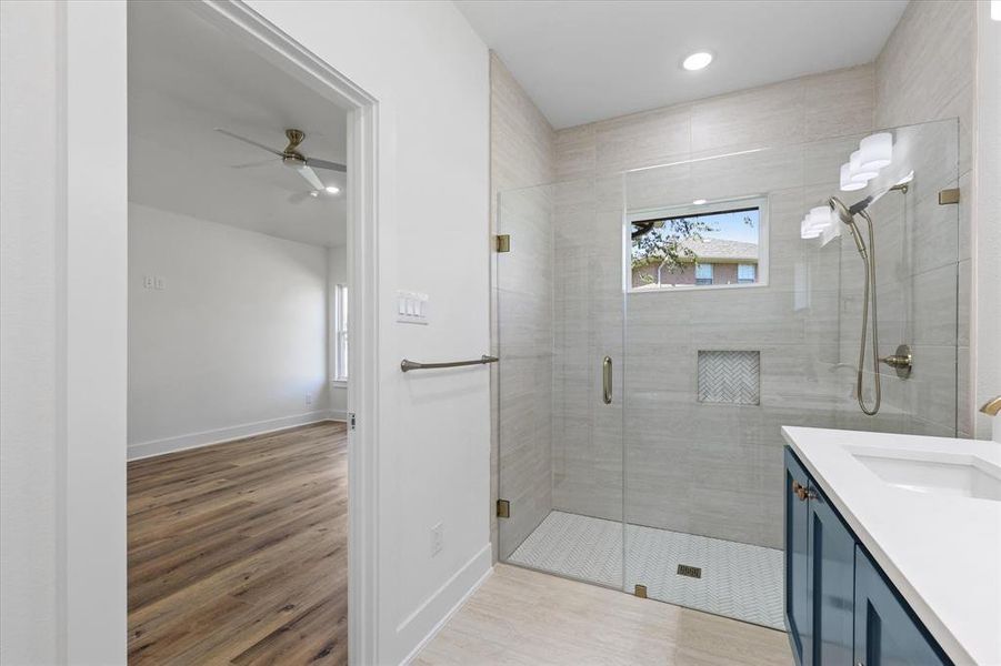 Bathroom featuring a shower with shower door, vanity, ceiling fan