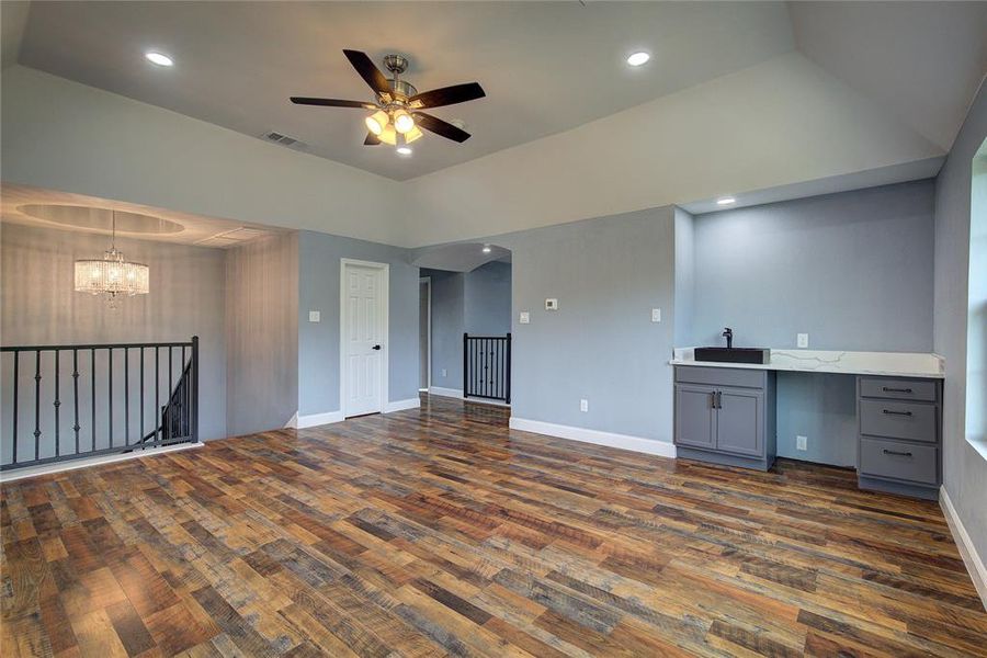 Unfurnished living room featuring dark hardwood / wood-style floors, ceiling fan with notable chandelier, and a raised ceiling