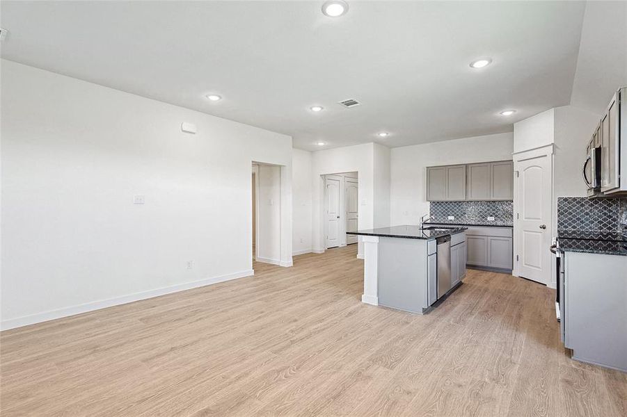 Kitchen featuring gray cabinetry, light hardwood / wood-style flooring, sink, a center island with sink, and tasteful backsplash