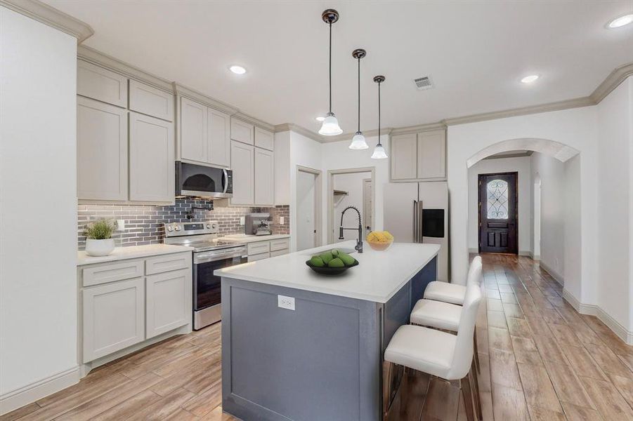 Kitchen with stainless steel appliances, crown molding, light wood-type flooring, and an island with sink