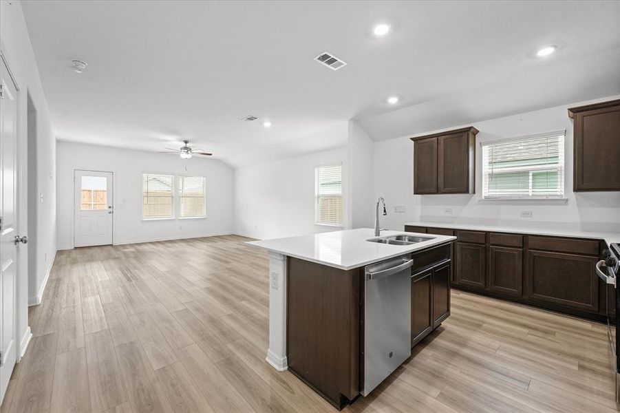 Kitchen with ceiling fan, light wood-type flooring, sink, dishwasher, and a kitchen island with sink