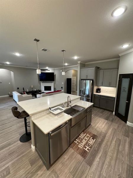Kitchen featuring hanging light fixtures, hardwood / wood-style flooring, fridge, a kitchen island with sink, and dishwashing machine